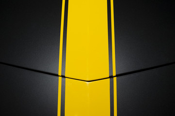 Surface of black sport sedan car, metal hood with yellow vertical lines, part of vehicle bodywork 