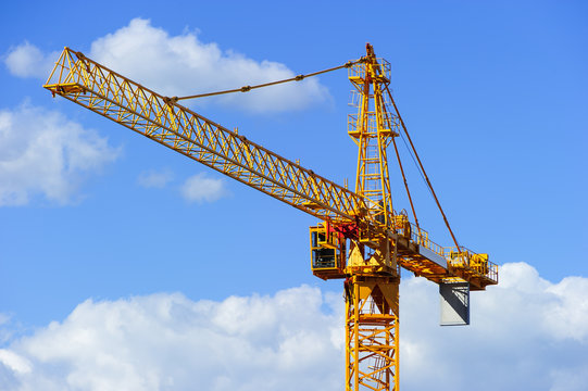 Yellow construction tower crane isolated on blue sky with white clouds background 