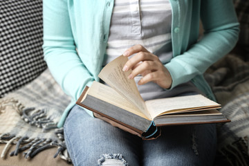 Young woman reading book, close-up, on home interior background