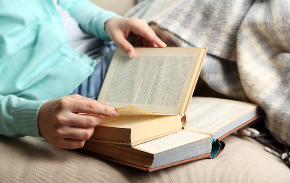 Young woman reading book, close-up, on home interior background