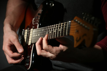Young man playing on electric guitar close up