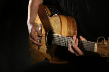 Fototapeta na wymiar Young man playing on acoustic guitar on dark background