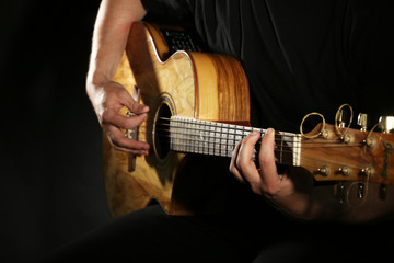 Young man playing on acoustic guitar on dark background