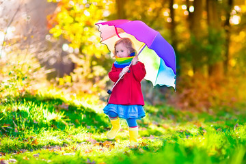 Child playing in the rain with umbrella in autumn park