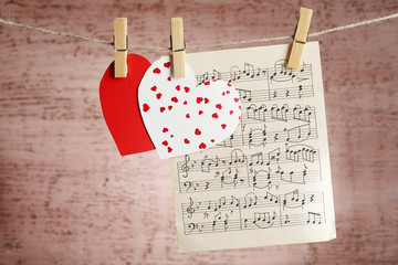 Bright hearts and music sheet hanging on rope on wooden background