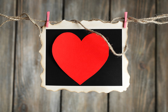 Bright heart on photo paper hanging on rope on wooden background