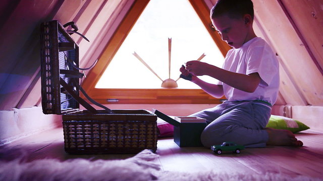 A little boy withdrawing toys from a chest in his attic room