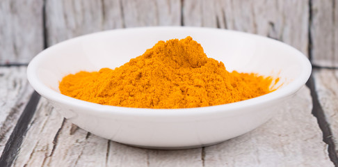 Turmeric powder in white bowl over rustic wooden background