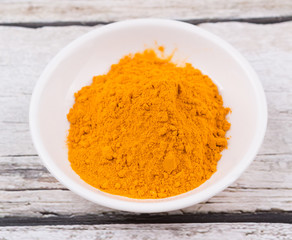 Turmeric powder in white bowl over rustic wooden background