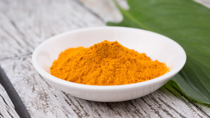 Turmeric powder and turmeric leaves over rustic wooden background