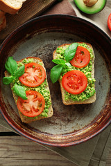 Vegan sandwich with avocado and vegetables on pan, on wooden background