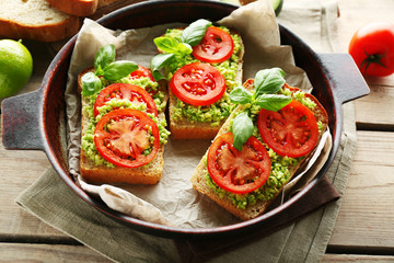 Vegan sandwich with avocado and vegetables on pan, on wooden background