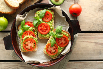 Vegan sandwich with avocado and vegetables on pan, on wooden background