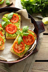 Vegan sandwich with avocado and vegetables on pan, on wooden background