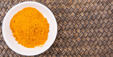 Turmeric powder in white bowl over wicker background