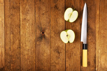 Halves of apple with knife on wooden background