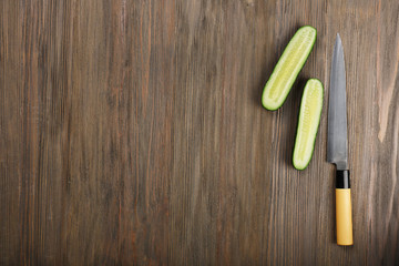 Halves of cucumber with knife on wooden background