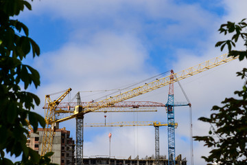 Cranes and building construction against blue cloudy sky. Focus