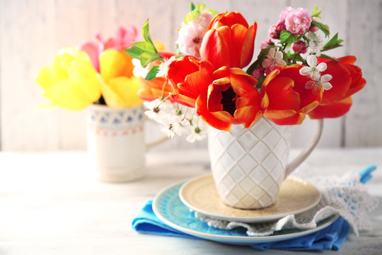 Spring bouquet in colorful mugs on color wooden background