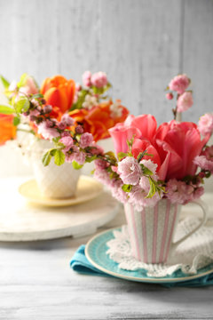 Spring bouquet in colorful mugs on color wooden background