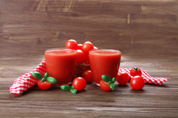 Glasses of tomato juice with vegetables on wooden background