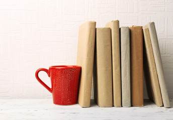 Books and cup on wooden shelf on wallpaper background