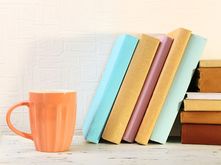 Obraz na płótnie Canvas Books and cup on wooden shelf on wallpaper background