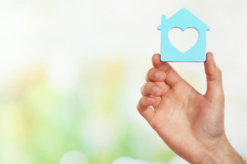 Female hand holding house on light blurred background
