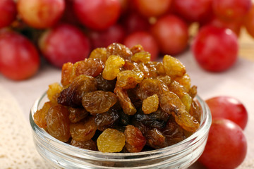 Raisins in bowl with grapes on table close up