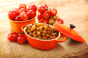 Raisins in bowl with grapes on table close up
