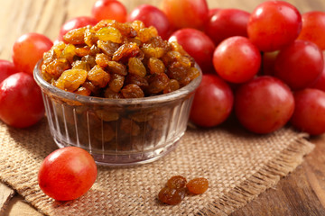 Raisins in bowl with grapes on table close up