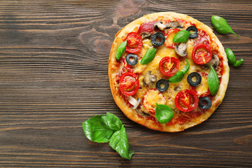 Tasty pizza with vegetables and basil on wooden background
