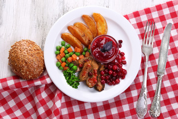 Beef with cranberry sauce, roasted potato slices, vegetables on plate, close-up