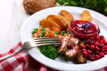 Beef with cranberry sauce, roasted potato slices, vegetables on plate, on color wooden background