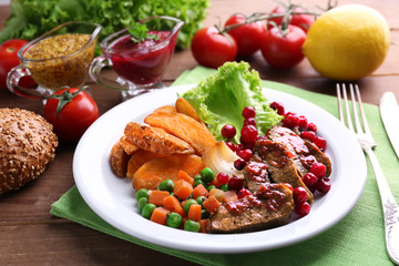 Beef with cranberry sauce, roasted potato slices, vegetables on plate, on  wooden background