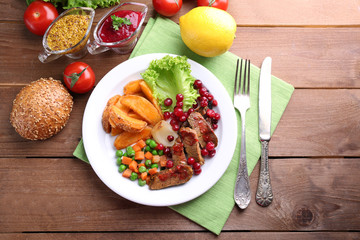 Beef with cranberry sauce, roasted potato slices, vegetables on plate, on  wooden background