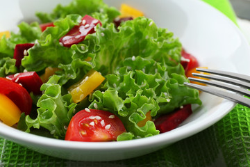 Bowl of fresh green salad on table with napkin, closeup