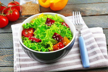 Bowl of fresh green salad on table with napkin, closeup