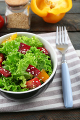 Bowl of fresh green salad on table with napkin, closeup