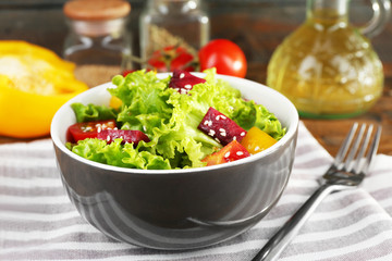 Bowl of fresh green salad on table with napkin, closeup