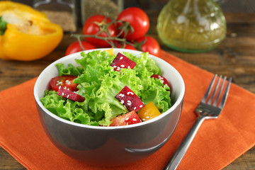 Bowl of fresh green salad on table with napkin, closeup