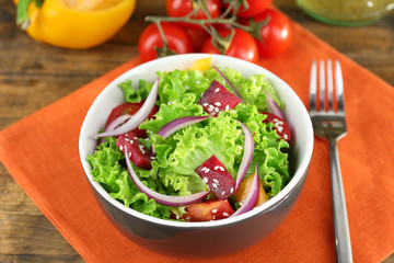 Bowl of fresh green salad on table with napkin, closeup
