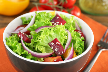 Bowl of fresh green salad on table with napkin, closeup