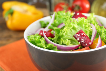 Bowl of fresh green salad on table with napkin, closeup