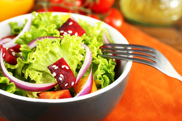 Bowl of fresh green salad on table with napkin, closeup