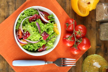 Bowl of fresh green salad on table with napkin, closeup
