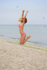 Jumping happy girl on the beach, fit sporty healthy sexy body in bikini, woman enjoys wind, freedom, vacation, summertime fun concept