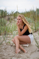 Obraz premium Outdoor portrait of melancholy and sad young pretty woman sitting on the sand near the sea alone