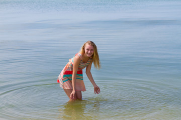 Teen happy girl in colorful dress posing in the sea; enjoys water, freedom, vacation, summertime fun concept