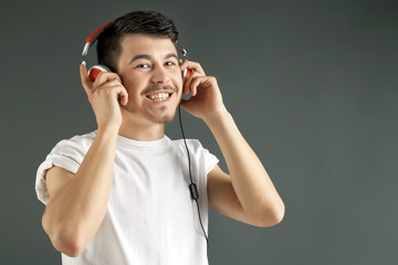 Handsome young man listening to music on grey background